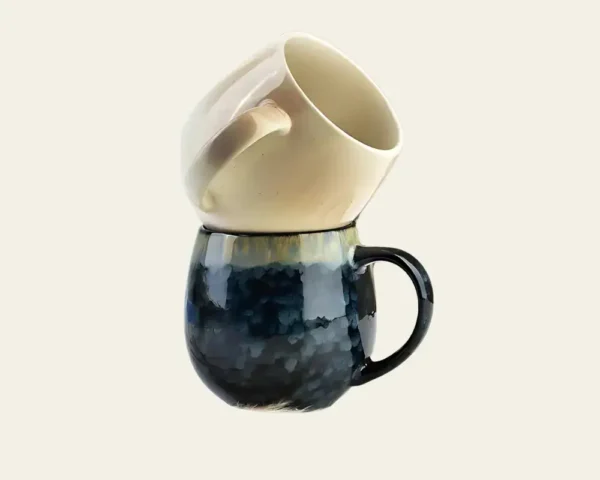 Dwa ceramiczne kubki, jeden na drugim, na tle jasnego tle, idealne do domowego użytku i relaksu.
