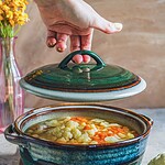 Szklany kapturek na ceramicznej garnku z warzywami, idealny do domowych zup i gulaszy, elegancki design, ręczna ceramika, rustykalny klimat kuchni, funkcjonalne naczynie do gotowania i podawania potraw.