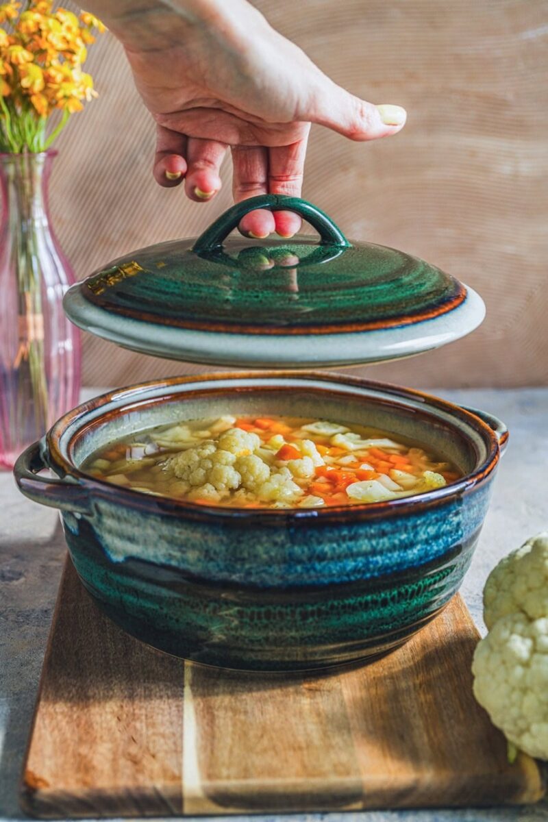 Szklany kapturek na ceramicznej garnku z warzywami, idealny do domowych zup i gulaszy, elegancki design, ręczna ceramika, rustykalny klimat kuchni, funkcjonalne naczynie do gotowania i podawania potraw.