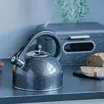 Stalowy czajnik z emaliowaną powierzchnią na kuchennym blacie z lemonami i chlebem, w stylu domowego zacisznego wnętrza z akcentami zdrowej kuchni i naturalnych produktów.