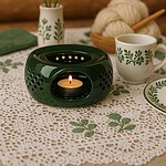 Ciepła dekoracyjna lampka z świecą w ceramicznym naczyniu, zestaw z filiżankami i serwetką na rustykalnym stole z kwiatami, idealny do domowego zakątka relaksu i odpoczynku.