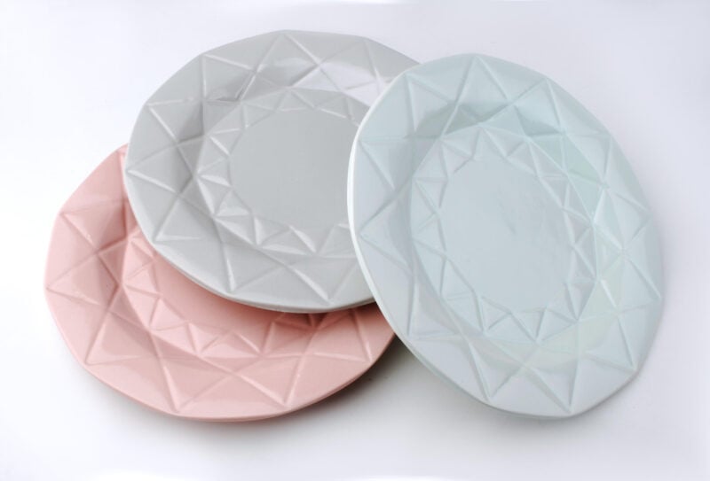 Trzy talerze ceramiczne w pastelowych kolorach z geometrycznym wzorem na krawędziach, idealne do dekoracji wnętrz i serwowania potraw w domu.