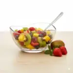 Świeża sałatka owocowa z kiwi, truskawkami, winogronami i mango w szklanej misce na jasnym tle.