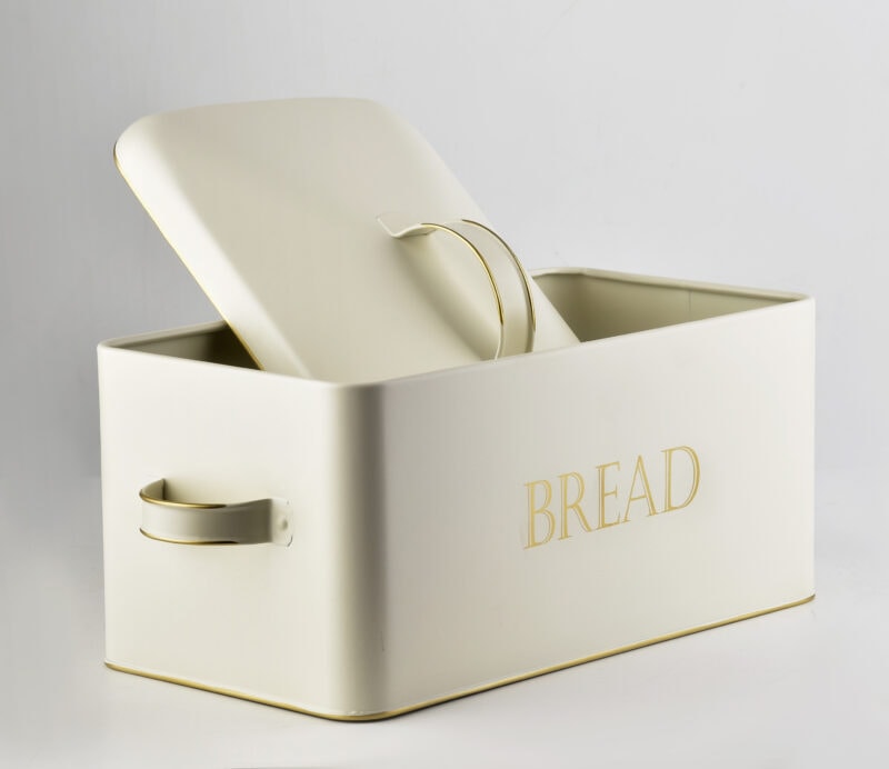 Metalowa skrzynka na chleb w jasnym odcieniu z ozdobnym złotym napisem "BREAD" idealna do przechowywania pieczywa w domu. Funkcjonalna i elegancka, świetnie pasuje do nowoczesnej kuchni i stylowych wnętrz.