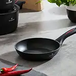 Porcelanowa patelnia do smażenia Valdinox na szarym blacie kuchennym z czerwonymi papryczkami i rośliną w czarnym naczyniu, idealna do domowych dań i codziennych posiłków.