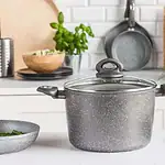 Akademia kuchni czarny garnek z pokrywką na białym blacie w nowoczesnej kuchni z białymi szafkami i akcesoriami kuchennymi.