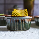 Nowoczesne ceramiczne naczynie do pieczenia z ręcznie zdobionym wzorem i żółtym ręcznikiem kuchennym w tle, idealne do domowych wypieków i serwowania potraw.