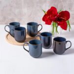 Ceramiczne kubki w odcieniach niebieskiego z brązowymi rączkami i wewnętrzną barwą, zestaw na drewnianej tacy, dekoracja z czerwonych kwiatów, idealne do codziennego użytku domowego, kolekcja Domowy Zakątek.