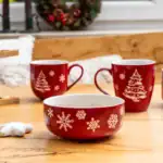 Czerwone kubki z świątecznymi motywami choinek i śnieżynek, idealne na Boże Narodzenie, ustawione na drewnianym stole w domowym zaciszu.