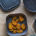 Chrupiące frytki ułożone w pojemniku na tle kafelków kuchennych, przekąska w stylu domowego gotowania, potrawa z frytek, popularne danie na rodzinne obiady, łatwe do przygotowania w domu.