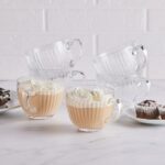 Przezroczyste szklanki do kawy i herbaty na białym tle, z biszkoptem i muffinkami w tle, idealne do domu, nowoczesny design, eleganckie naczynia, akcesoria kuchenne, domowe przyjęcia, zestaw na każdą okazję.