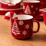 Czerwony kubek z motywem świątecznym, choinką i śnieżynkami, ozdobiony małym candy cane. Idealny na bożonarodzeniowe okazje, dodaje magii i ciepła do domowego zakątka w okresie świątecznym.