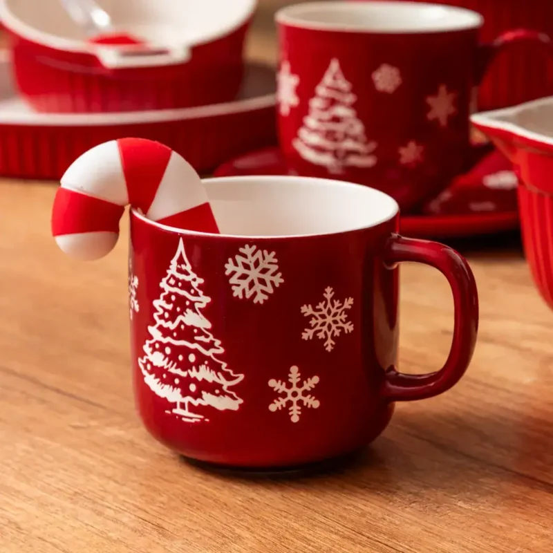 Czerwony kubek z motywem świątecznym, choinką i śnieżynkami, ozdobiony małym candy cane. Idealny na bożonarodzeniowe okazje, dodaje magii i ciepła do domowego zakątka w okresie świątecznym.