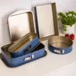 Metalowe foremki do pieczenia, blaszane formy do ciasta, zestaw do pieczenia w odcieniach niebieskiego, łagodne światło, domowa atmosfera, akcesoria kuchenne, idealne do pieczenia ciast i ciasteczek, funkcjonalny zestaw do pieczenia z klamrami, nowoczesny design, praktyczne rozwiązania dla domowych cukierników.