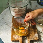 Miska do mieszania składników z jajkiem, w kuchni, na drewnianej desce, w tle szklana miarka z mąką, białe pozostałości na powierzchni, kreatywne gotowanie, domowe wypieki, rustykalna atmosfera, przyjemne gotowanie.