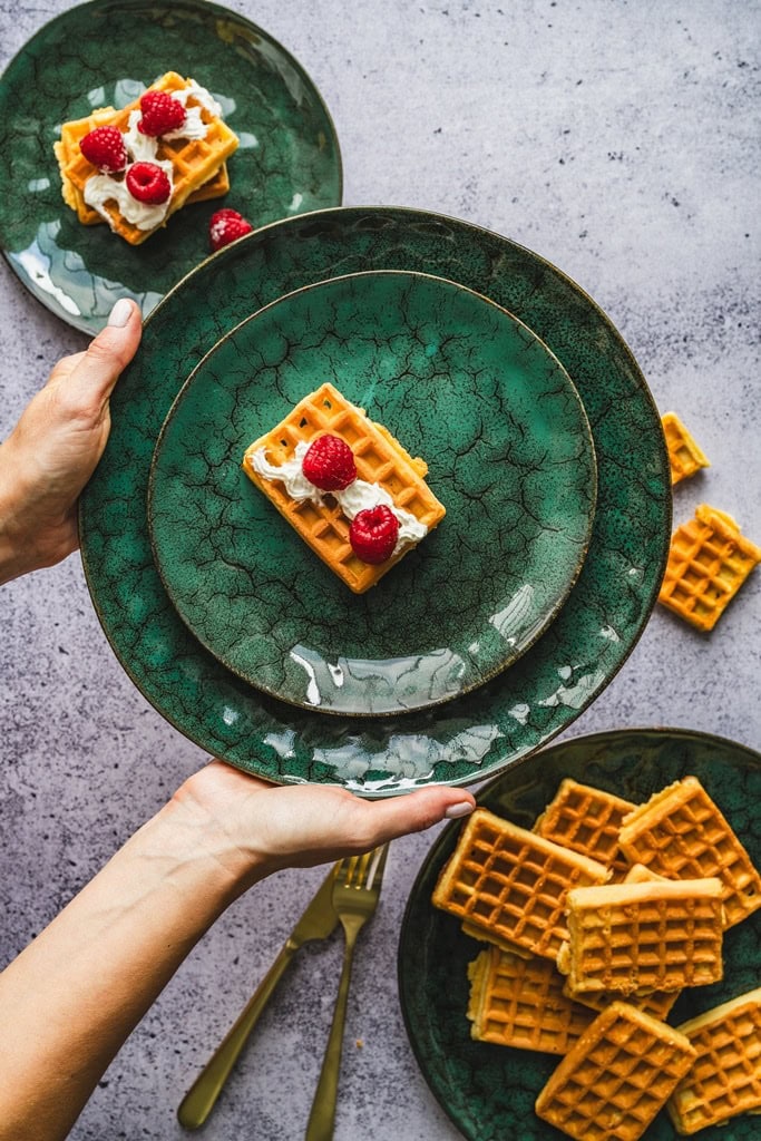 Waffle z bitą śmietaną i malinami na zielonym talerzu, deser domowy, słodka przekąska, sezonowe owoce, domowy zakątek, eleganckie nakrycie, komfortowe jedzenie.