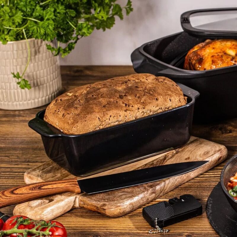 Chleb domowy w formie ceramicznej na drewnianej desce z warzywami i nożem, pieczywo wypiekane w domu, naturalny chleb z piekarnika, zdrowe i smakowite wypieki, dekoracja kuchni, domowe wypieki, domowy zakątek.