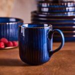 Ceramiczna filiżanka w głębokim odcieniu niebieskiego z teksturą pionowych pasków, idealna do kawy lub herbaty, element eleganckiej zastawy stołowej w domowym zaciszu.