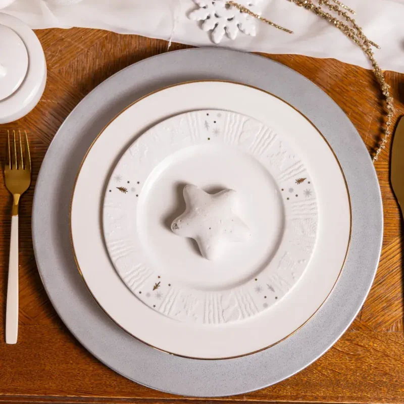Dobrawa bożonarodzeniowa, świąteczny stół z eleganckim zastawieniem, porcelanowe talerze z motywami świątecznymi, dekoracje na święta, zimowa atmosfera, dekoracje świąteczne, świąteczny wystrój stołu, domowe dekoracje na Boże Narodzenie.