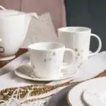 Biała filiżanka z zimowym motywem świątecznym na talerzyku, idealna do herbaty w domowym zakątku, elegancka i dekoracyjna, świąteczne akcesoria, elegancka zastawa stołowa, domowe wnętrza, bożonarodzeniowy klimat.