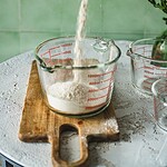 Mąka wsypana do miarki pomiarowej, domowe wypieki, naturalne składniki, kuchnia ekologiczna, Przepis na zdrowie i smaczne potrawy, Domowy Zakątek, zdrowe gotowanie, składniki do pieczenia, zrównoważona dieta, kuchnia bio, ekologiczne produkty, inspiracje kulinarne.