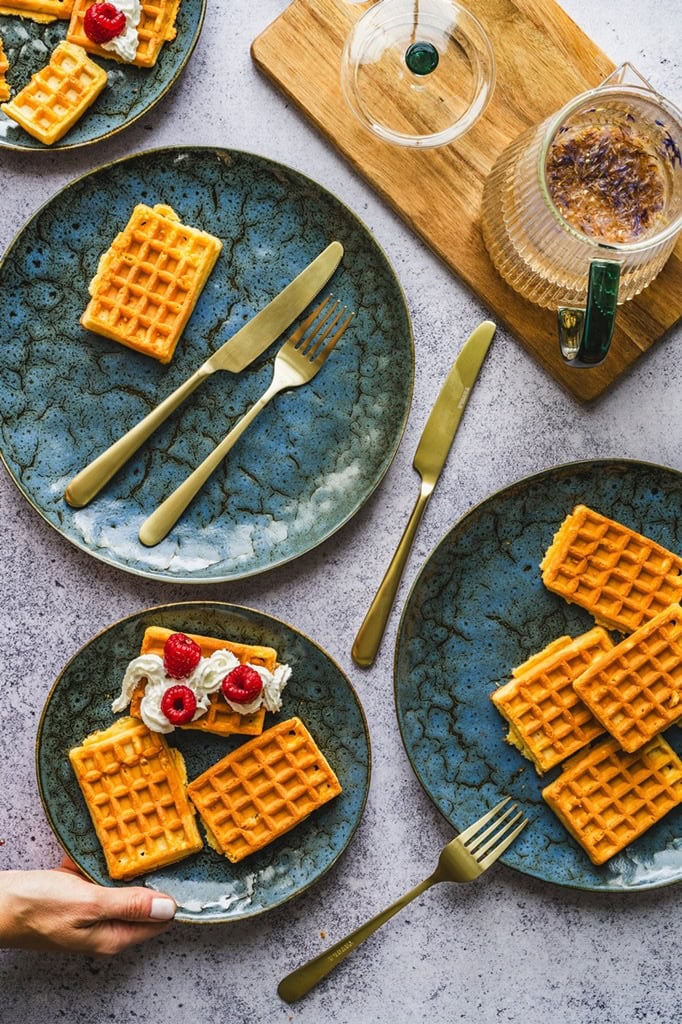 Delikatne gofry na talerzach w bliskim ujęciu, podawane z bitą śmietaną i truskawkami, elegancki deser na śniadanie lub brunch, stylowa zastawa i naturalne światło, tabliczka i czajnik w tle, rustykalny klimat, domowe wypieki, zdrowe i pyszne przekąski, elegancka prezentacja, Pinterest food photography.