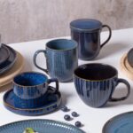 Ceramiczne kubki i talerze w niebieskich odcieniach z złotymi zdobieniami, idealne na domowe śniadania i kawę, elegancki zastaw kuchenny dla miłośników wyjątkowego designu.