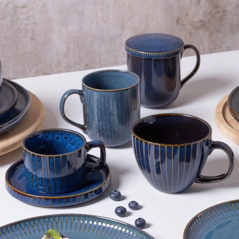 Ceramiczne kubki i talerze w niebieskich odcieniach z złotymi zdobieniami, idealne na domowe śniadania i kawę, elegancki zastaw kuchenny dla miłośników wyjątkowego designu.