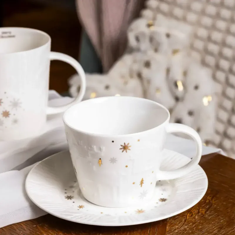 Biała ceramiczna filiżanka z zimowym wzorem, na talerzyku z motywem świątecznym, idealna na zimowe wieczory, kategoria Domowy Zakątek, dekoracje i kuchnia na święta.