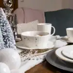 Delikatna zastawa świąteczna z białym wzorem, idealna na bożonarodzeniowe stoły, dekoracje z choinkami i złotymi dodatkami, tworzy ciepłą i elegancką atmosferę podczas świąt.