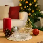 Szklana misa z dekoracyjnymi wzorami śnieżnych kryształów na świątecznym stole, obok czerwona świeca, szyszka i ornament, w tle choinka z bombkami, nastrojowa atmosfera bożonarodzeniowa.