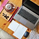 Pracujący laptop na drewnianym stole z notesem, myszką i filiżankami z kawą lub herbatą, idealne do pracy z domu, zbliżenie, domowy zakątek, produktywność, komfortowe warunki pracy w domu.
