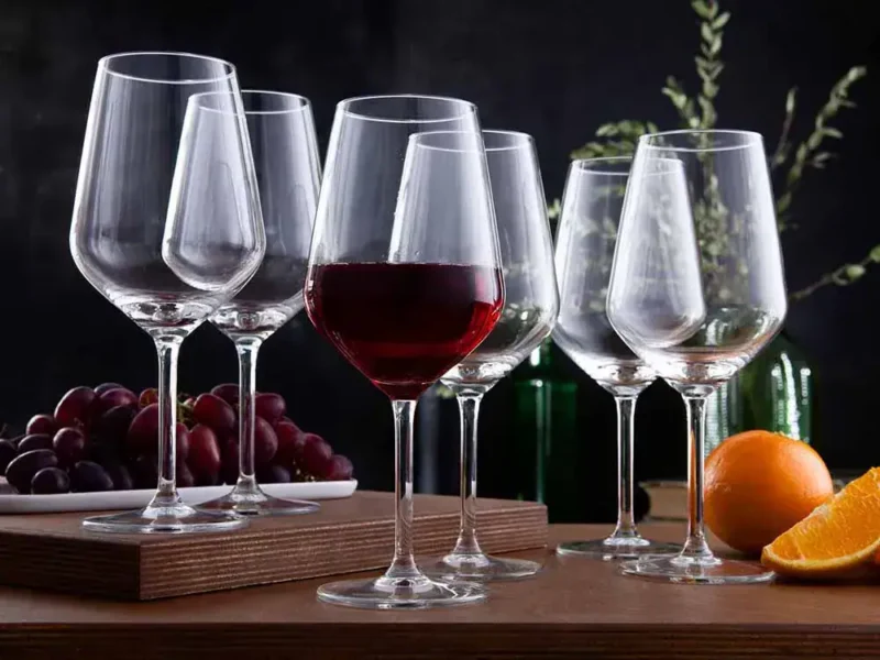 Wysokiej jakości kieliszki do wina czerwonego i białego, na drewnianym blacie z winogronami i pomarańczą, eleganckie prezentacje do domowego zacisza, idealne na relaks z winem.