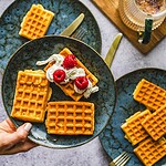 Delikatne gofry z bitą śmietaną i malinami na ceramicznym talerzu, idealne na śniadanie lub deser, domowy klimat, smaczne i chrupiące.
