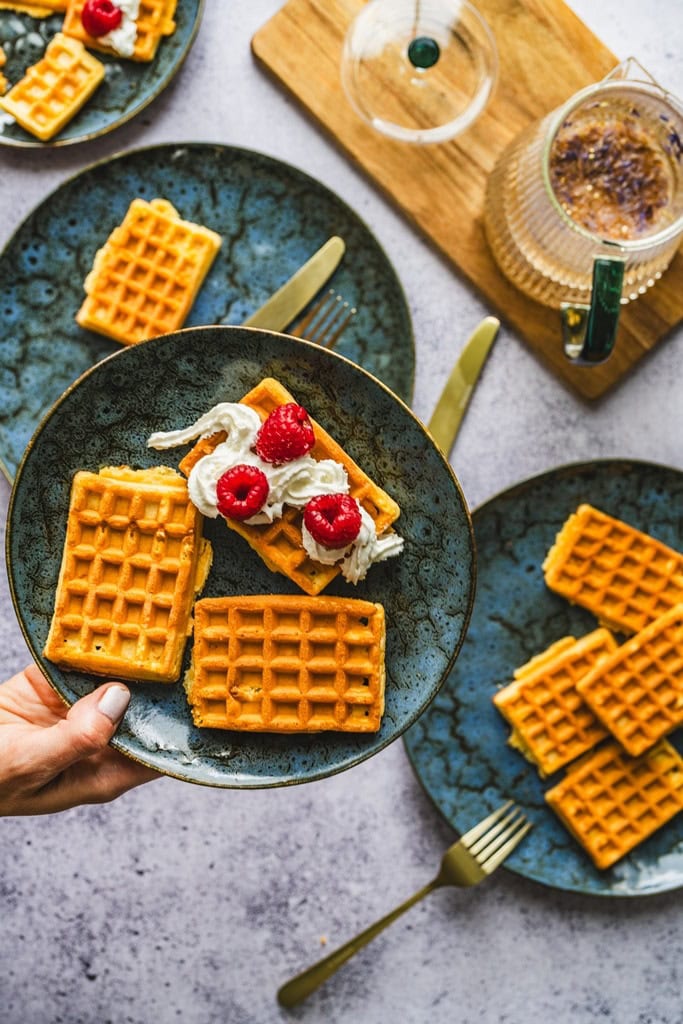 Delikatne gofry z bitą śmietaną i malinami na ceramicznym talerzu, idealne na śniadanie lub deser, domowy klimat, smaczne i chrupiące.
