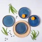 Ceramiczne talerze w odcieniach niebieskiego z metalicznym wykończeniem, zestaw na drewnianej tacy, z kawałkami mandarynki i jagód, dekoracja w stylu domowego zakątka do serwowania potraw.