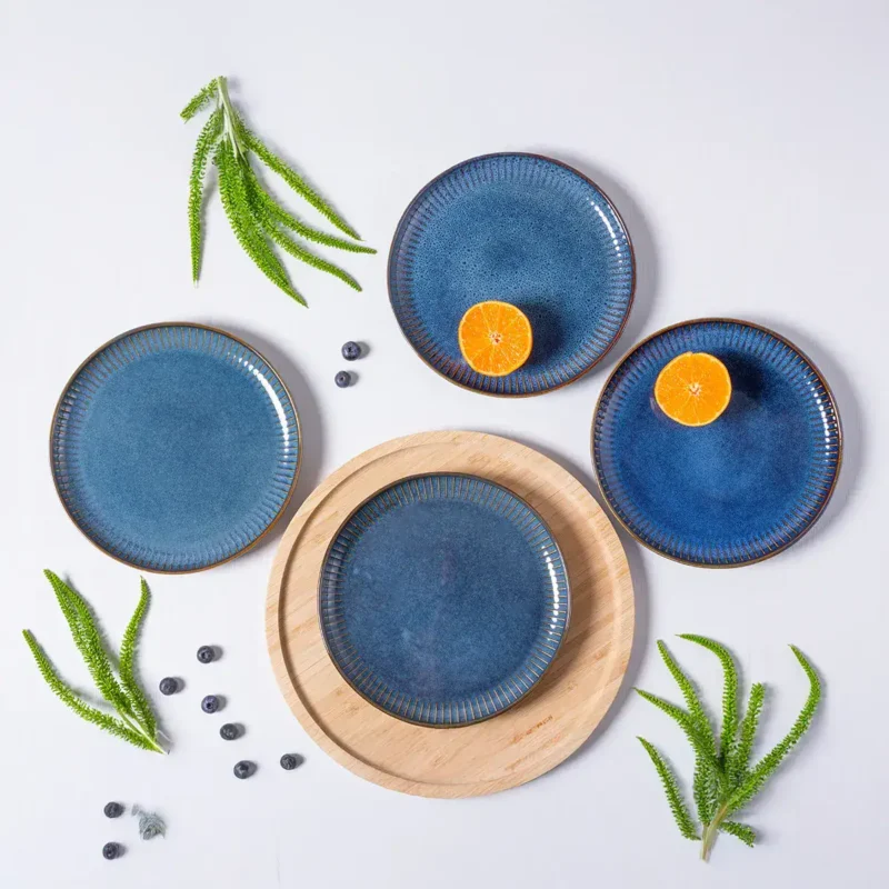 Ceramiczne talerze w odcieniach niebieskiego z metalicznym wykończeniem, zestaw na drewnianej tacy, z kawałkami mandarynki i jagód, dekoracja w stylu domowego zakątka do serwowania potraw.