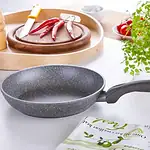 Czarna patelnia granitowa na kuchennym blacie, nowoczesny sprzęt kuchenny, płyta indukcyjna, świeże zioła i warzywa, domowe gotowanie, produkty kuchenne dla zdrowego stylu życia.