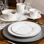 Wyrafinowana zastawa stołowa na świąteczny obiad, eleganckie talerze i kubki z delikatnym wzorem śnieżynek i choinek, idealna na bożonarodzeniowe spotkania w Domowym Zakątku.