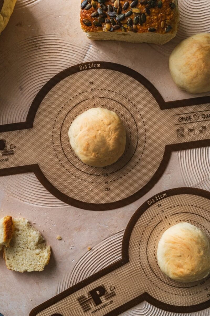 Miękkie ciasto na bazie naturalnych składników, gotowe do pieczenia, na stole kuchennym z funkcjonalną matą do wyrabiania i formowania wypieków, idealne do pieczenia chleba i bułek.