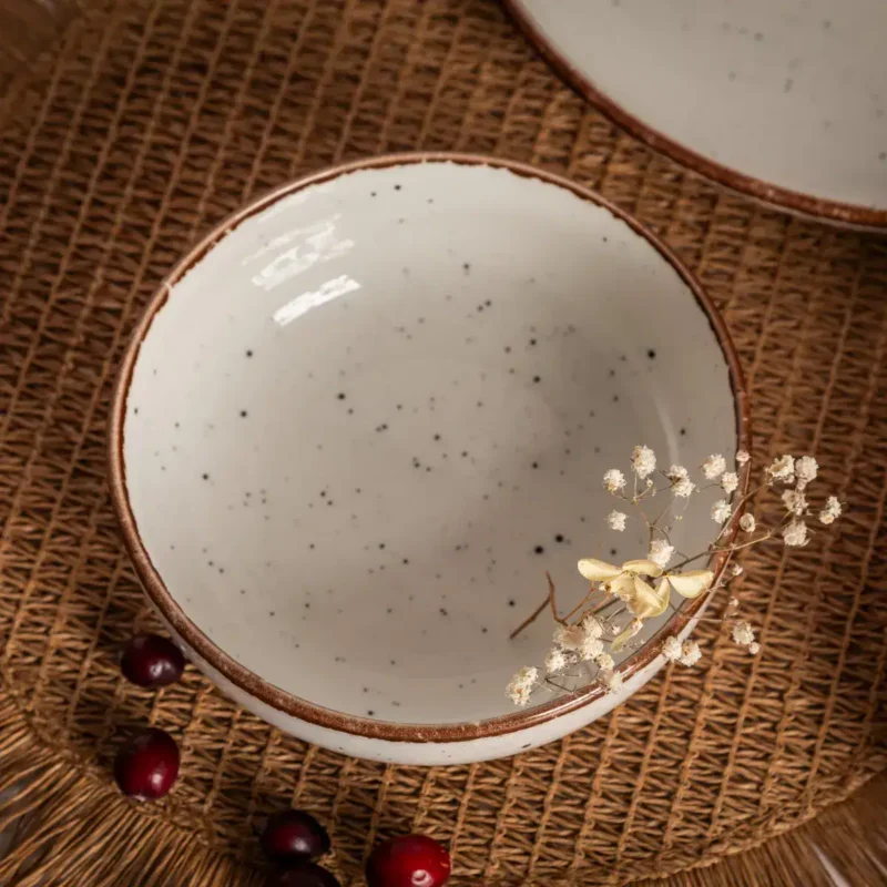 Naturalny ceramiczny kubek z czarnym kropeczkami, idealny do kawy i herbaty, na naturalnej teksturze wiklinowego dywanika, ozdobiony suchymi kwiatami i gałązkami, odzwierciedlenie domowego stylu.