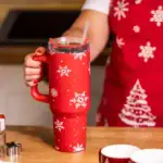 Czerwony kubek termiczny z śnieżynkami, trzymający napój w kuchni, idealny na zimowe dni, z nadrukiem świątecznym, wykończenie w stylu domowego zakątka.