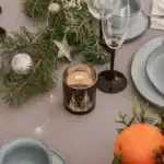 Zestaw świąteczny na eleganckim stole z dekoracjami bożonarodzeniowymi, świecami, szkłem i porcelaną, idealny na świąteczną kolację, klimat Domowy Zakątek, bożonarodzeniowa aranżacja, stylowa dekoracja stołu, elegancki wystrój.