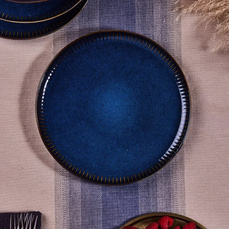 Srebrny talerz ceramiczny w głębi niebieskim odcieniu z dekoracyjnymi złotymi wykończeniami, idealny do eleganckiego stołu, inspirowany stylem Domowego Zakątka, nadaje się na wyjątkowe okazje.
