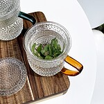 Schwarzebloggermętna herbata miętowa w szklance na drewnianej podstawce, z liśćmi mięty, elegancke i naturalne zestawienie do relaksu i zdrowego stylu życia.